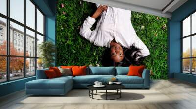 Portrait of beautiful african american woman laying on green grass in park Wall mural