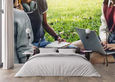 Group of smiling international students or teenagers sitting and using laptop computer doing their homework with book together in park at university.Education and friendship Concept Wall mural