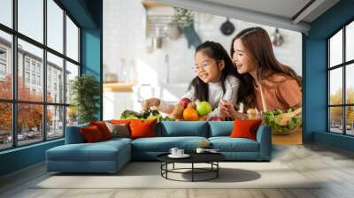 Portrait of enjoy happy love asian family mother with little asian girl daughter child having fun help cooking food healthy eat together with fresh vegetable salad ingredient in kitchen Wall mural