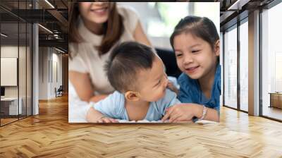 Portrait of enjoy happy love family asian mother playing with adorable little asian baby and sister girl, newborn, infant.Mom touching care with cute son in a white bedroom.Love of family concept Wall mural