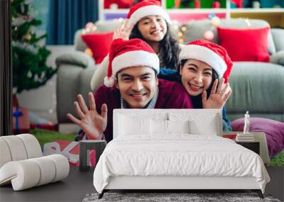 Portrait of happy family father and mother with daughter in santa hats having fun smiling at camera waving and saying hello to you and enjoying spending time together in christmas time at home Wall mural