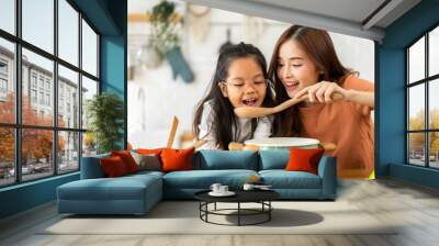 Portrait of happy love asian family mother with little asian girl daughter child help cooking food healthy eat with fresh vegetable testing smell soup in a pot with spoon.helping mommy in kitchen Wall mural