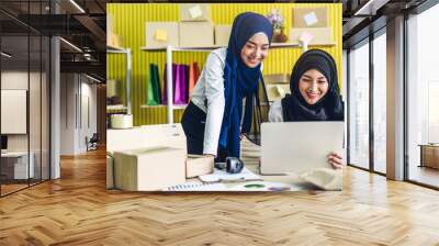 Portrait of smiling beautiful two muslim owner asian woman freelancer sme business online shopping working on laptop computer with parcel box on table at home - Business online shipping and delivery Wall mural