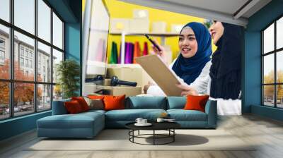 Portrait of smiling beautiful two muslim owner asian woman freelancer sme business online shopping working on laptop computer with parcel box on table at home - Business online shipping and delivery Wall mural