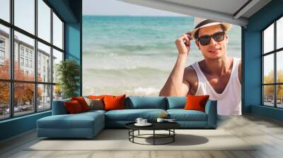 Portrait of smiling happy handsome man model enjoying and relax in fashionable sunglasses and hipster summer straw hat standing on the tropical beach and looking at camara.Summer vacations and travel Wall mural