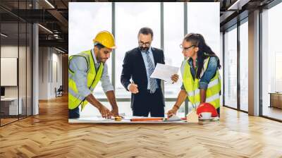 Professional of team engineers cargo foreman in helmets working with blueprint and construction tools on table at the construction site Wall mural