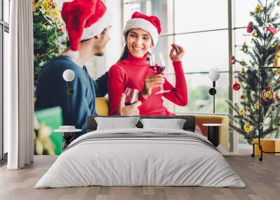 Romantic sweet couple in santa hats having fun and drinking wine glasses while celebrating new year eve and enjoying spending time together in christmas time at home Wall mural