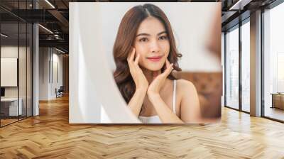 Smiling of young beautiful pretty asian woman clean fresh healthy white skin looking at mirror.asian girl touching on her face with hand and applying cream at home.spa and beauty concept Wall mural