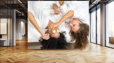 Two diverse women relaxing with cucumber slices on eyes wearing white robes in a spa setting enjoying skincare treatment, self-care routine, beauty and wellness, happy and relaxed, spa day experience Wall mural