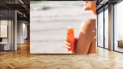 Woman wearing two piece bikini applying suncream with sun drawn on back and holding sunscreen lotion on the tropical beach.Young girl with sun block skin protection.Summer vacations Wall mural