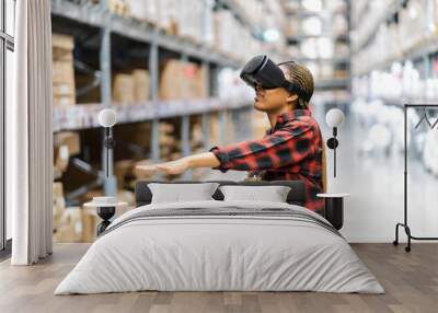 Young africn woman wearing virtual reality (VR) goggles stands in middle of warehouse with shelves stocked, traditional workwear and modern technology, technology logistics in industrial and warehouse Wall mural