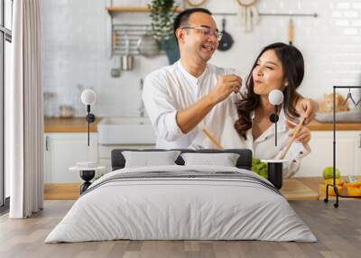 Young asian family couple having fun cooking and preparing cook vegan food healthy eat with fresh vegetable salad on counter in kitchen at home.Happy couple looking to preparing food Wall mural