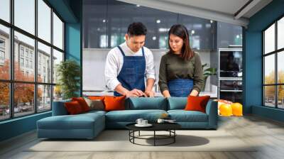 Young asian family couple having fun cooking and preparing cook vegan food healthy eat with fresh vegetable salad on counter in kitchen at home.Happy couple looking to preparing food Wall mural