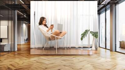 Young smiling happy beautiful asian woman relaxing using laptop computer in the bedroom at home.Young creative girl working and typing on keyboard.work from home concept Wall mural