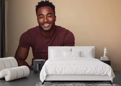 Smiling Black man in casual attire sitting against a beige background, exuding confidence and warmth Wall mural