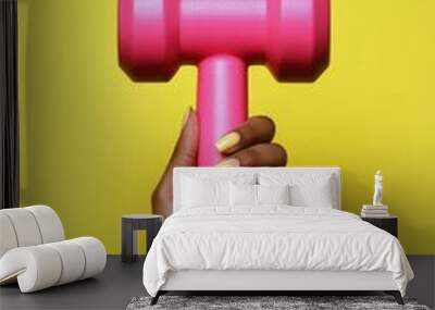 A person holds a bright pink dumbbell against a cheerful yellow background during a workout Wall mural