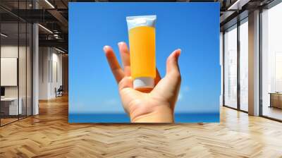 a woman's hand is holding a tube of sunscreen with a sky view Wall mural