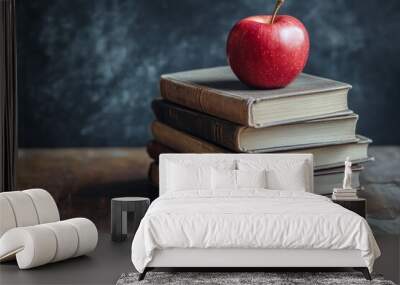 An apple resting on vintage books stacked on a wooden surface against a dark backdrop Wall mural