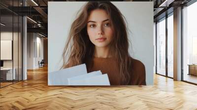 Young woman holding blank papers in a neutral setting during daylight hours Wall mural