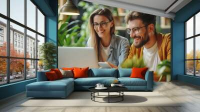 cheerful colleagues with technology in green cafe. two joyful colleagues use a laptop and smartphone Wall mural