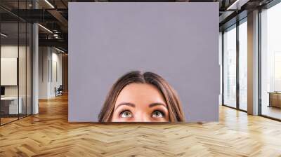 Closeup beautiful young woman looking up on blank copy space isolated on gray background. Attractive funny girl staring above her head. Half face of adorable woman thinking about solution. Empty space Wall mural