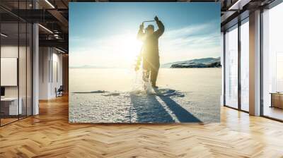 Fisherman drills a hole in the ice of a large frozen lake on a sunny day. The joy of winter fishing Wall mural