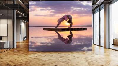 graceful gymnast performs a flexible pose at sunset in the reflection of the water beautiful silhouette Wall mural