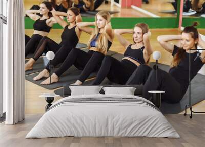 Group of athletic adult women performing sit up exercises to strengthen their core abdominal muscles at fitness training Wall mural