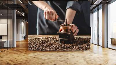 Hands baristas in a dark apron grind on a manual grinder fragrant coffee beans. Selection of fresh coffee for espresso Wall mural