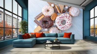 Harmful sweet foods on wooden background. Donuts, muffins, chocolates on the table pile. Unhealthy diet and overweight Wall mural