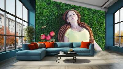 Modern young girl with a hairstyle dreadlocks in the Park on a green meadow eating apples and enjoying the autumn mood Wall mural