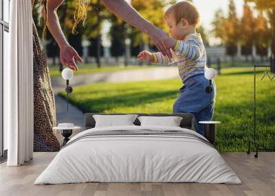 Mom helps cute baby walking on a green lawn in nature on a Sunny autumn day. Concept first child steps Wall mural