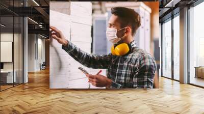 Portrait male foreman inspector in medical face mask and protective headphones checking woodwork stock at factory storage. Man supervisor counting wood inventory. Warehouse worker. COVID-19 quarantine Wall mural