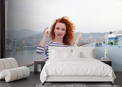 Portrait of a curly-haired red-haired girl on the background of high-rise buildings of the city. young beautiful girl on a background of the silhouette of the city posing in life style clothes Wall mural