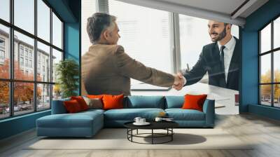 The two happy businessmen handshaking over a glass in the office Wall mural