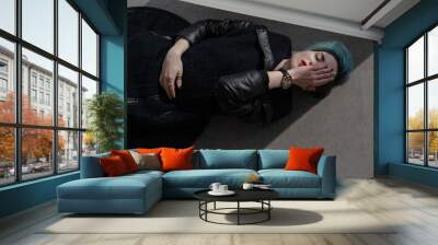 Top view of beautiful girl with short blue fashionable hairstyle in black coat. Model lying on the floor as a victim of violence. She covers half of face with hand, another hand on her stomach Wall mural