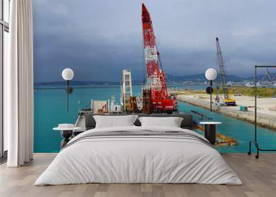 two huge excavators together synchronously on floating platforms in the blue water of the Pacific Ocean extract white sand from the bottom and load onto a barge amid clouds and tropical islands Wall mural