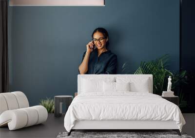 Beautiful young woman in casuals standing by a wall and talking on mobile phone Wall mural