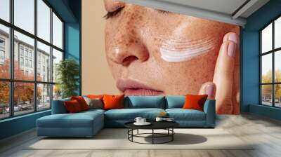 Close-up of female face with freckled skin. High-detailed shot of woman skin applying moisturizer. Wall mural