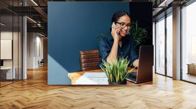 Entrepreneur sitting at table typing on a laptop while talking on cell phone  Wall mural