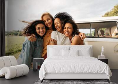 Four happy female friends laughing together standing in front of a van. Women enjoying summer road trip. Wall mural