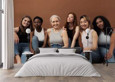 Group of six different women in casuals sitting together on brown background Wall mural