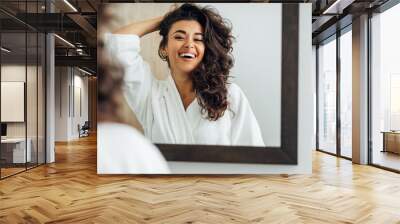 Happy woman in bathroom. Young female playing with her hair in front of a mirror. Wall mural