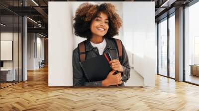 Portrait of a beautiful female college student leaning a wall and looking at camera Wall mural