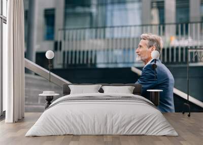 Side view of senior investor walking on stairs outside the office building in the city Wall mural