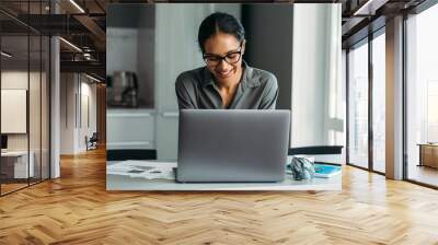 Smiling woman standing at the kitchen counter and working on a laptop computer from home Wall mural