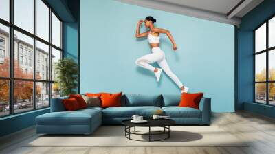 Sports woman running in studio. Full length shot of young female exercising over blue backgroud. Wall mural