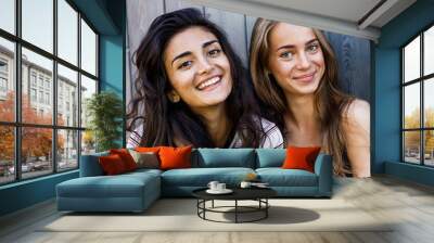 Two beautiful women looking at camera. Smiling friends standing at wall. Wall mural