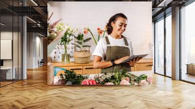 Young female florist making notes on a digital tablet. Woman checking online orders in shop. Wall mural