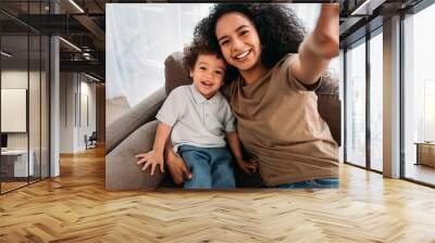 Young woman and her little son taking selfie. Happy mother with her kid sitting on a sofa. Wall mural